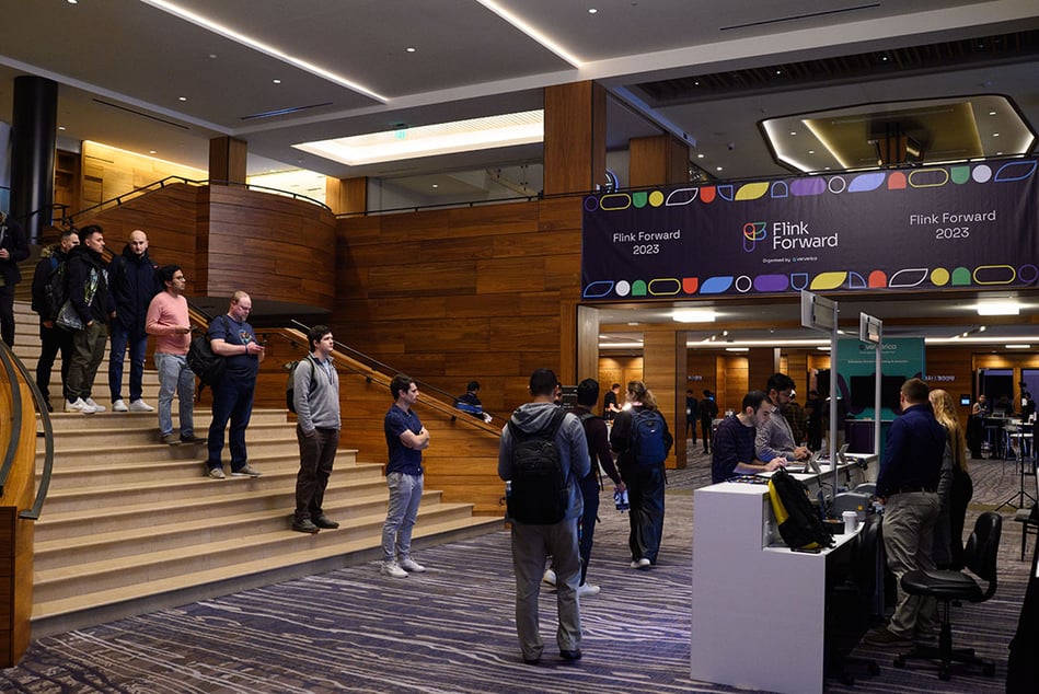 Flink Forward Seattle attendees arrive at the registration desk. Flink Forward sign behind people standing in line on stairs. 